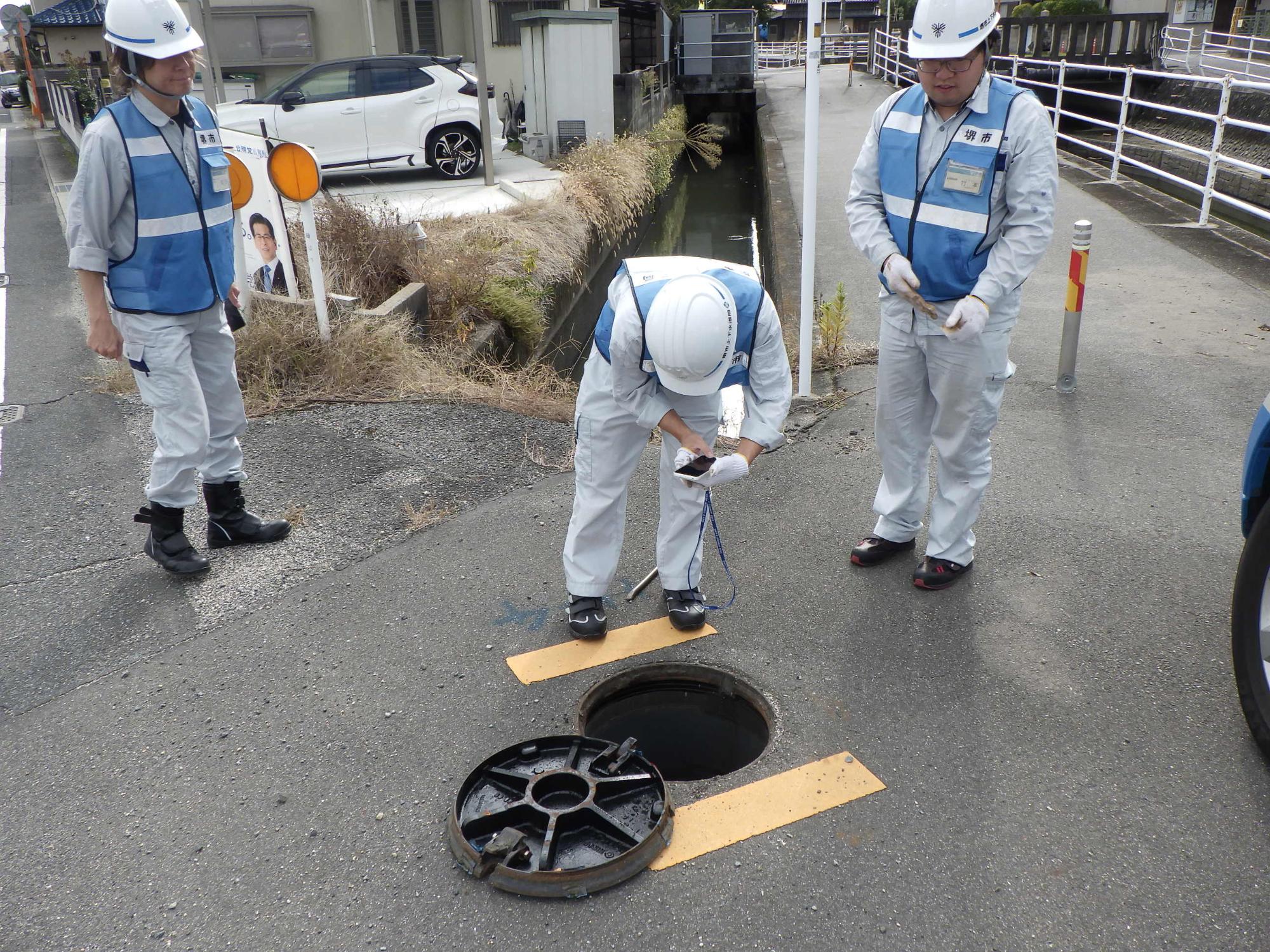 地面の消火栓マンホールの蓋を開けて音聴棒で漏水しているか音を聞く作業の写真